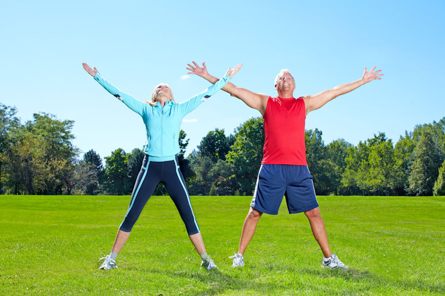 Active senior couple exercising outdoors with arms raised in a park.